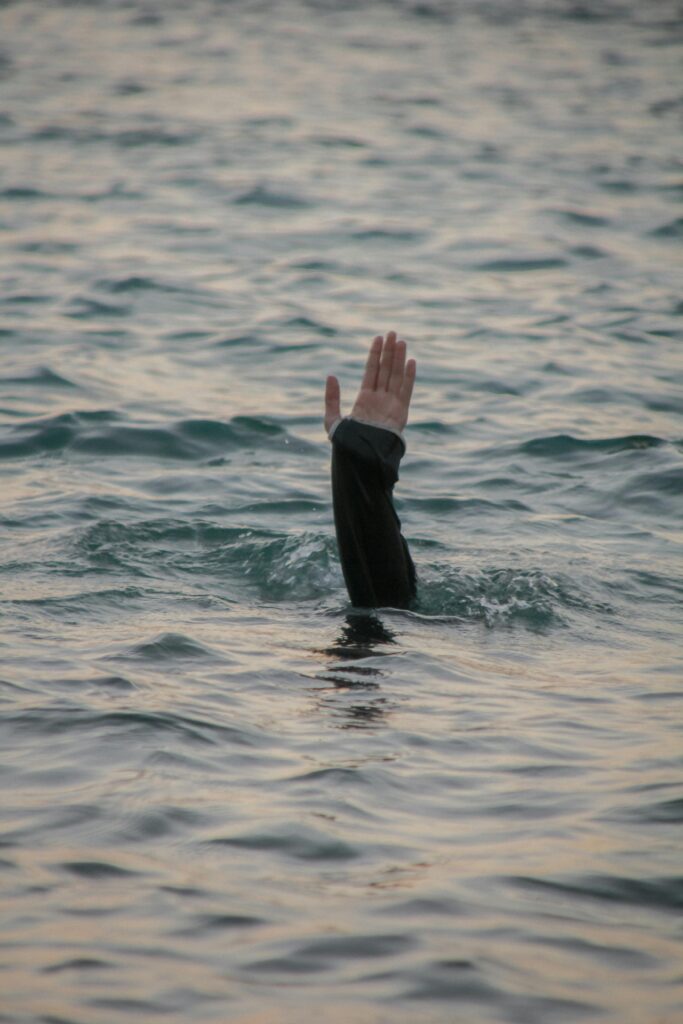 A lone hand emerges from ocean water, symbolizing a call for help or rescue in a calm sea.
